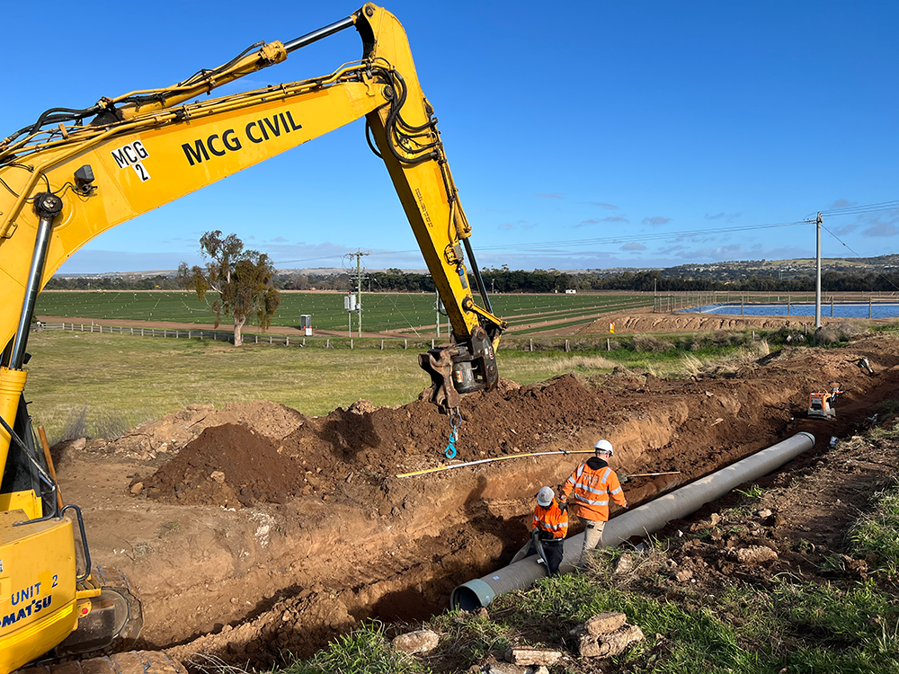 Excavator digging channel into a field for pipes