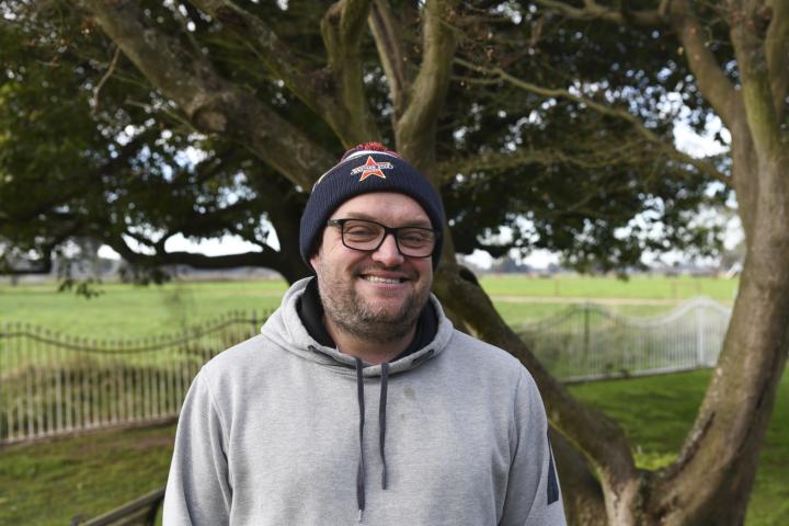 Smiling man in beanie and jumper standing in front of a tree