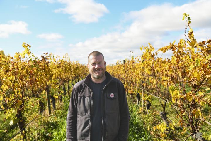 man standing in a vinyard smiling at the camera