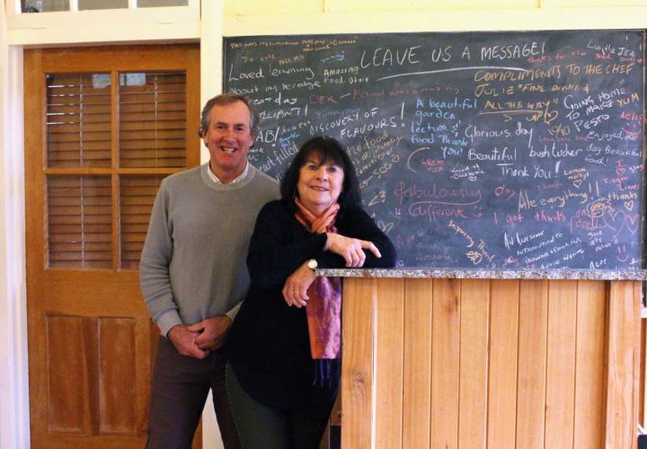 Woman and Man standing in front of a chalk board with colourful writing displayed. 
