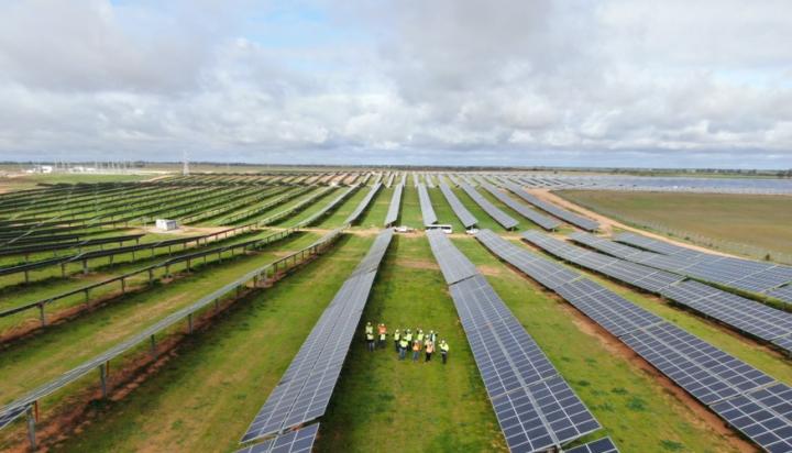 Aerial image of a large solar farm with people in high visibility clothing looking at the camera with their hands in the air.