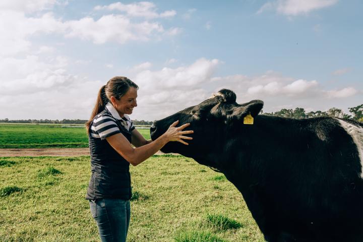 Smiling woman holding a cows face in a field