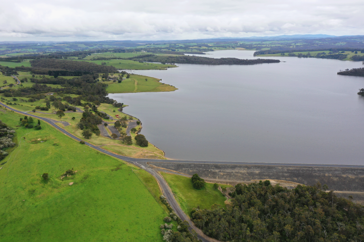 Image taken with drone of blue lake next to a road surrounded by green hills and trees