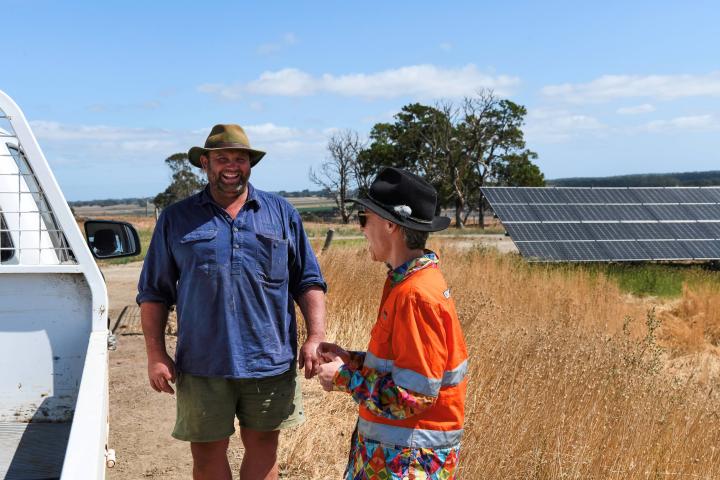 Man and women smiling while standing by a ute outside in a dry field